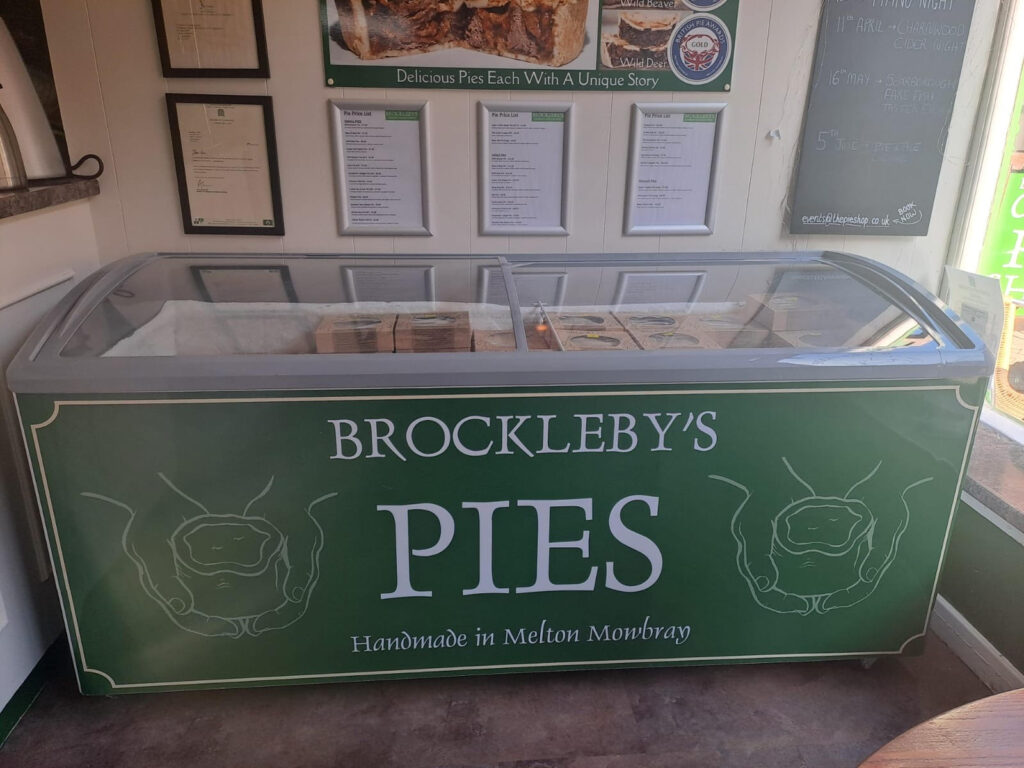 Artisan pie shop display featuring Brockleby’s Pies from Melton Mowbray, with a refrigerated counter full of boxed handmade pies, branded signage, award posters, and a chalkboard promoting upcoming food and drink events.