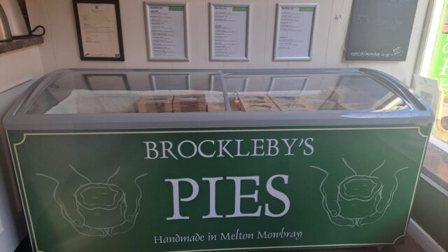 Artisan pie shop display featuring Brockleby’s Pies from Melton Mowbray, with a refrigerated counter full of boxed handmade pies, branded signage, award posters, and a chalkboard promoting upcoming food and drink events.