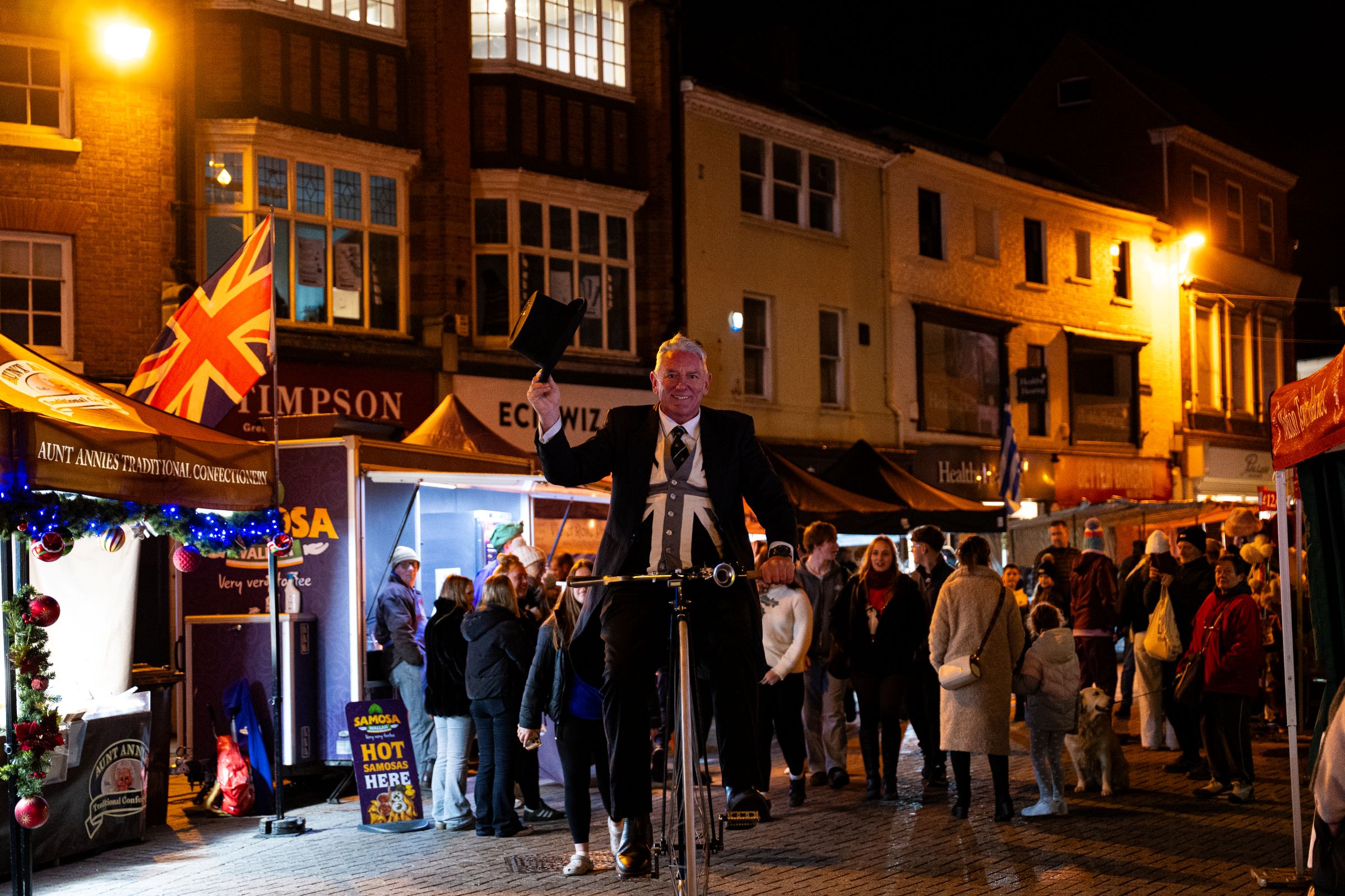 Man on a penny cycle in a town centre dressed in Victorian period costume