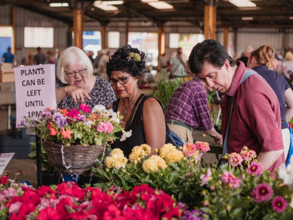 Visitors browsing colourful flowers and plants at an indoor market.