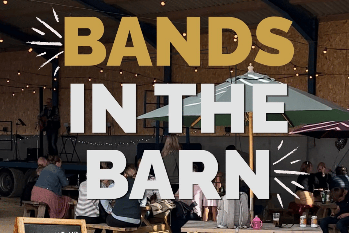 People in an open barn sitting at picnic benches. Display text - Bands in the barn.