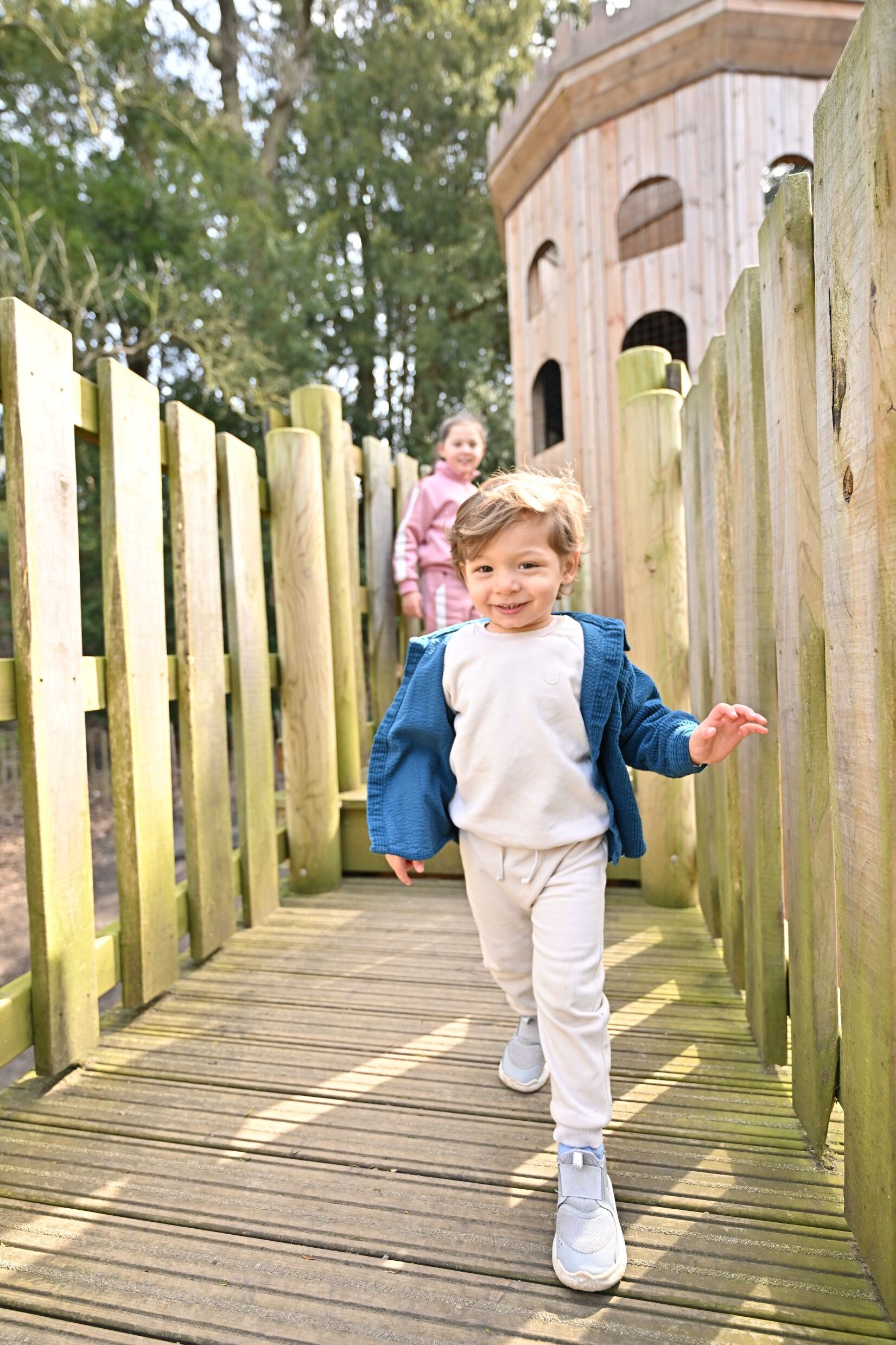 Small boy dressed in white with a blue jacket on a wooden playground structure