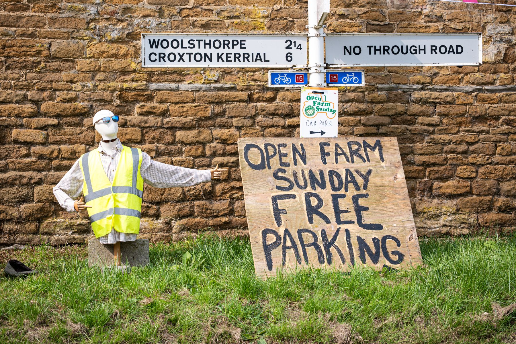 Mannequin in a high-vis vest pointing to a sign advertising “Open Farm Sunday” with free parking.