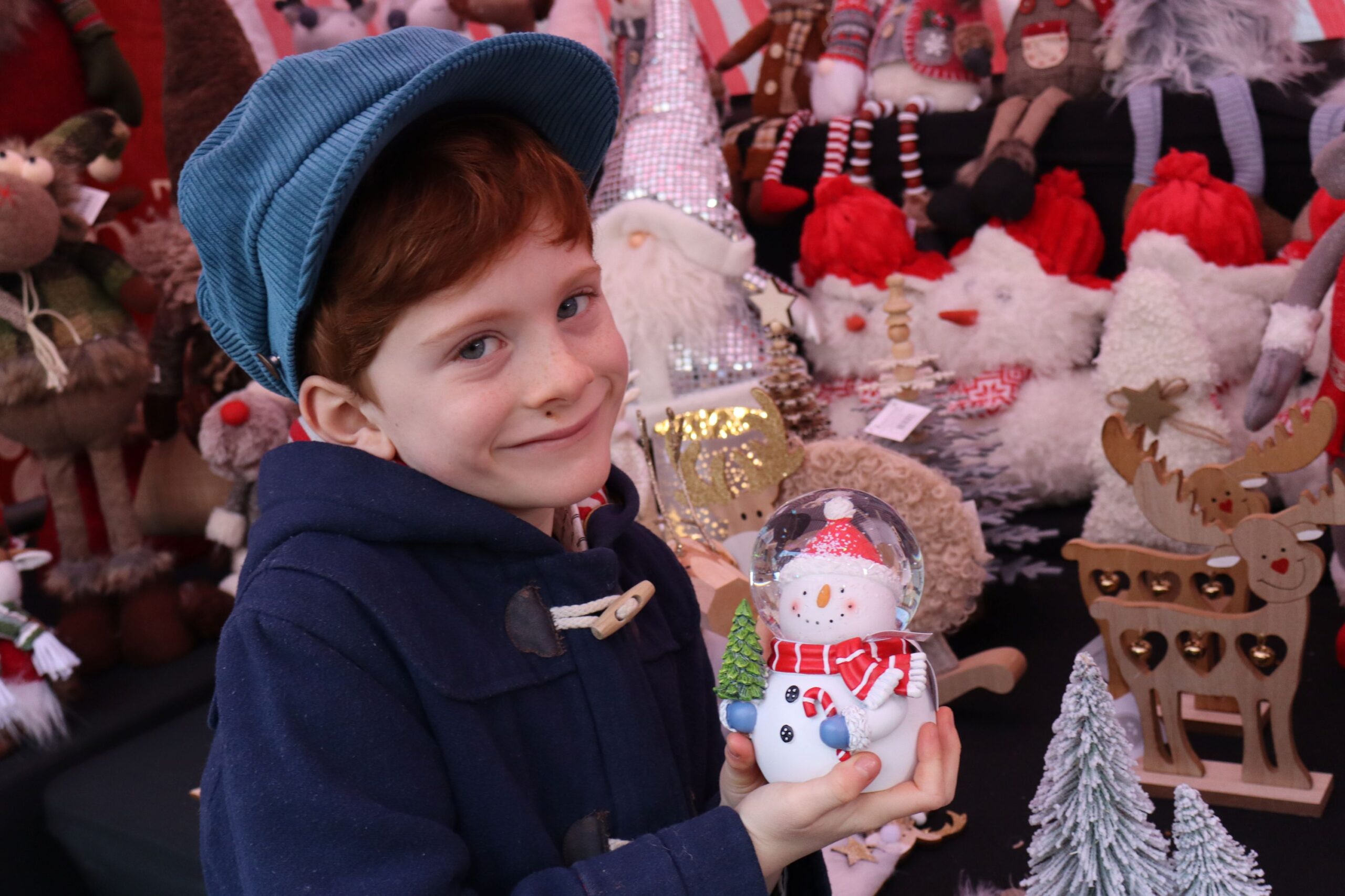 Child holding a snow globe at a festive Christmas market stall.