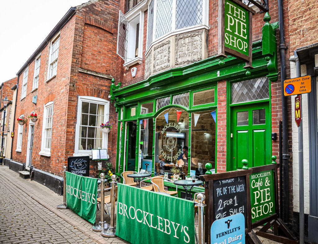 Exterior of Brockleby’s Pie Shop with green frontage, outdoor seating, and traditional brick buildings on a cobbled street.