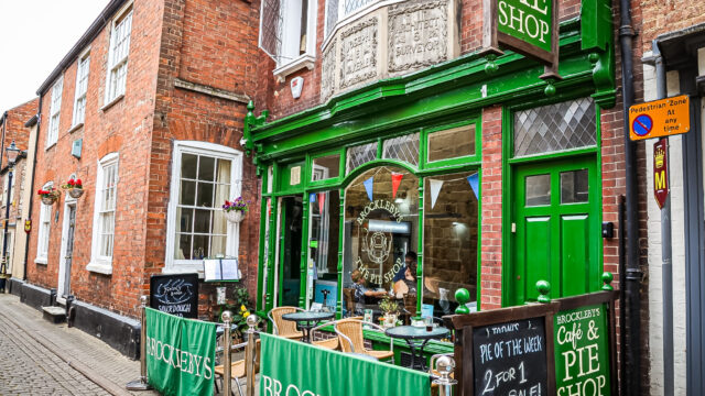 Exterior of Brockleby’s Pie Shop with green frontage, outdoor seating, and traditional brick buildings on a cobbled street.
